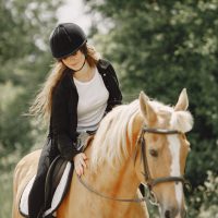 Rider woman riding her horse on a ranch. Woman has long hair and black clothes. Female equestrian touching her brown horse.